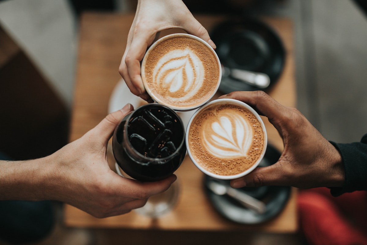 Three people touching coffee cups together over a table